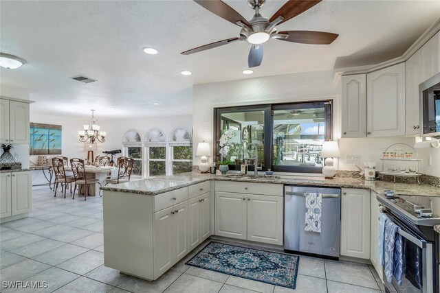 kitchen featuring kitchen peninsula, appliances with stainless steel finishes, an inviting chandelier, white cabinetry, and light tile patterned flooring