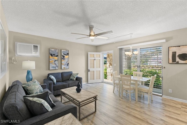 living room featuring a wall mounted AC, light hardwood / wood-style flooring, ceiling fan with notable chandelier, and a textured ceiling