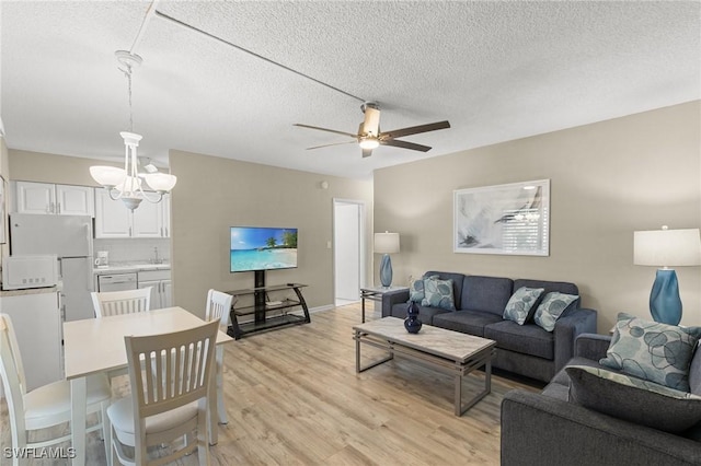 living room with ceiling fan with notable chandelier, a textured ceiling, and light hardwood / wood-style flooring