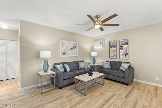 living room with a textured ceiling, light hardwood / wood-style flooring, a wall mounted AC, and ceiling fan