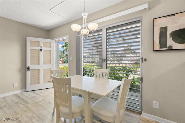 dining space with a textured ceiling, light hardwood / wood-style flooring, and a notable chandelier