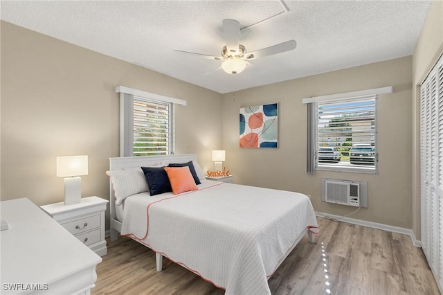 bedroom with a wall mounted air conditioner, light wood-type flooring, a textured ceiling, ceiling fan, and a closet