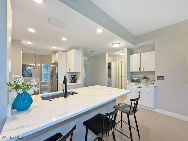 kitchen featuring stainless steel refrigerator, an inviting chandelier, kitchen peninsula, a kitchen bar, and white cabinets