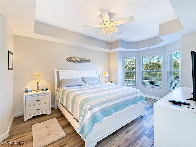 bedroom with a tray ceiling, ceiling fan, and dark wood-type flooring