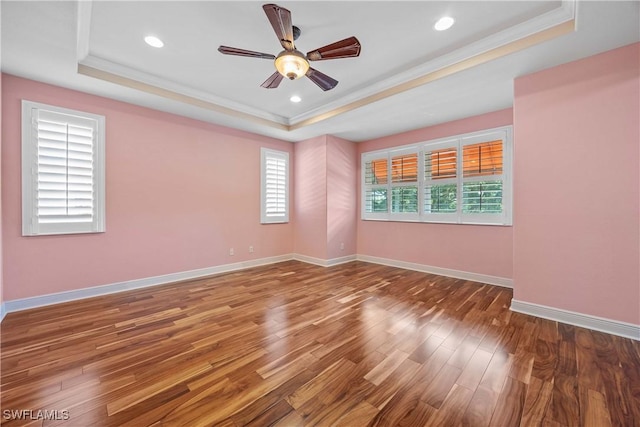 empty room with a tray ceiling, hardwood / wood-style flooring, ornamental molding, and ceiling fan