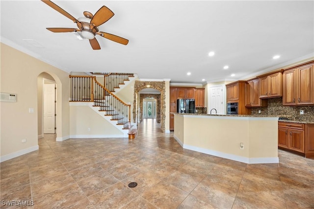 kitchen featuring black refrigerator, tasteful backsplash, stainless steel oven, a kitchen island with sink, and stone countertops