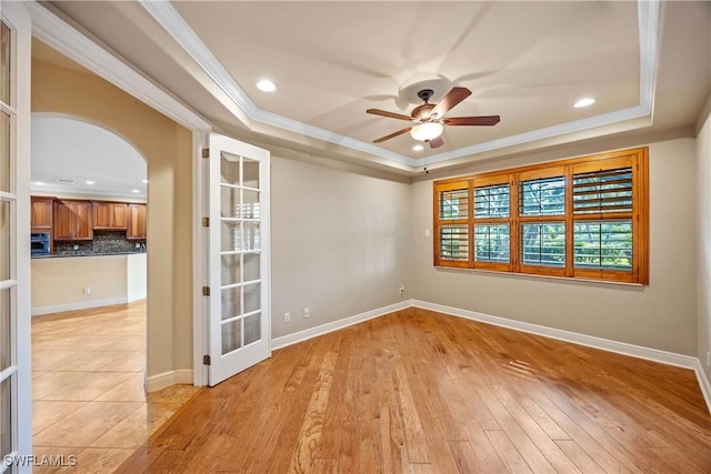 spare room with ceiling fan, light hardwood / wood-style floors, ornamental molding, and a tray ceiling