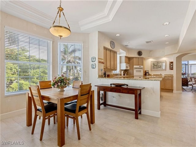 dining space with sink, a raised ceiling, and crown molding