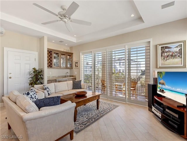 living room featuring a tray ceiling, bar, ceiling fan, and light hardwood / wood-style flooring