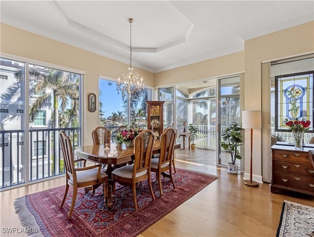 dining area with a raised ceiling, a wealth of natural light, light hardwood / wood-style floors, and an inviting chandelier