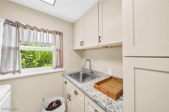 kitchen with light stone counters, white cabinetry, and sink