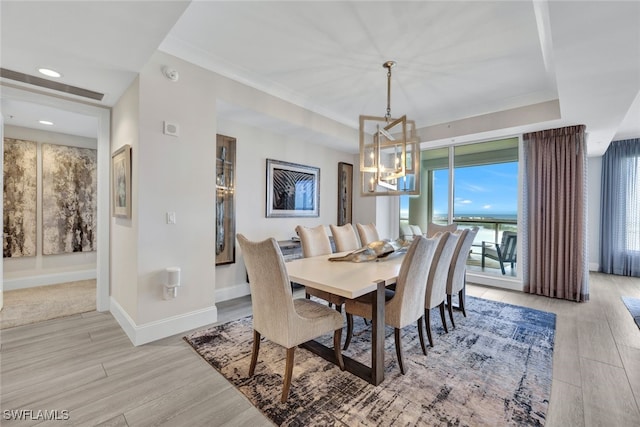 dining area with an inviting chandelier, a raised ceiling, and light wood-type flooring