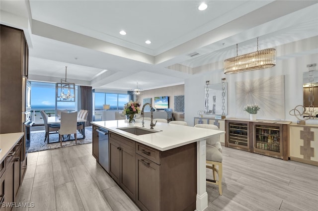 kitchen with sink, beverage cooler, hanging light fixtures, a kitchen island with sink, and a notable chandelier