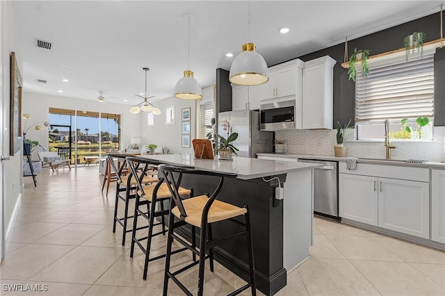 kitchen featuring hanging light fixtures, a kitchen island, light tile patterned flooring, white cabinets, and appliances with stainless steel finishes