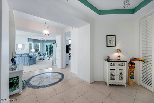 corridor with light tile patterned floors, a tray ceiling, and a notable chandelier