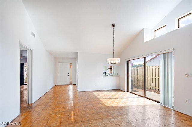 empty room with light parquet flooring, high vaulted ceiling, a healthy amount of sunlight, and a notable chandelier