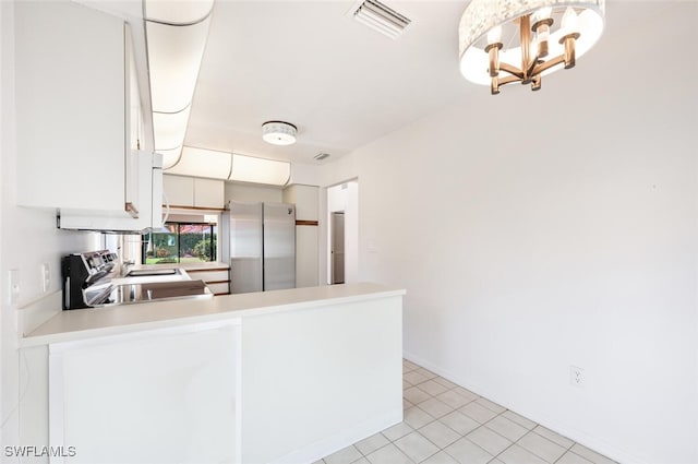 kitchen with kitchen peninsula, appliances with stainless steel finishes, light tile patterned floors, a notable chandelier, and white cabinets