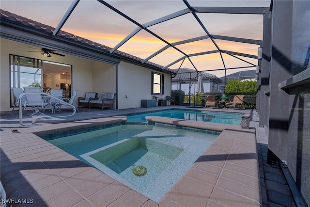 pool at dusk featuring glass enclosure, a patio area, and an in ground hot tub