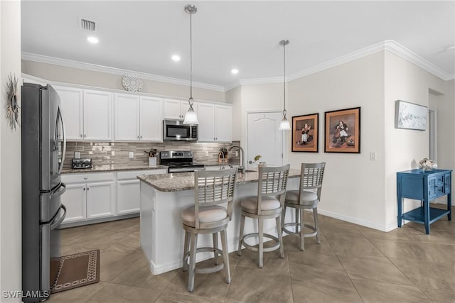 kitchen featuring hanging light fixtures, appliances with stainless steel finishes, white cabinetry, and a kitchen island with sink