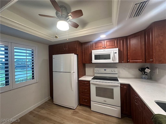 kitchen with backsplash, white appliances, a raised ceiling, and light wood-type flooring