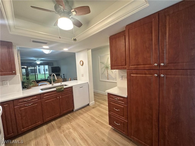 kitchen with light wood finished floors, white dishwasher, a tray ceiling, light countertops, and a sink