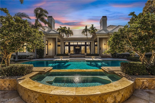 pool at dusk featuring an in ground hot tub