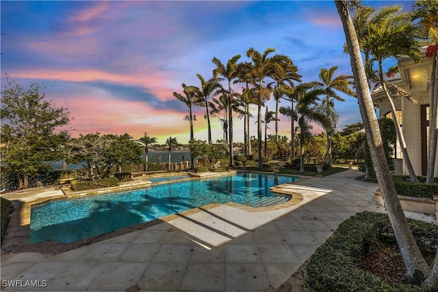 pool at dusk featuring an in ground hot tub and a patio