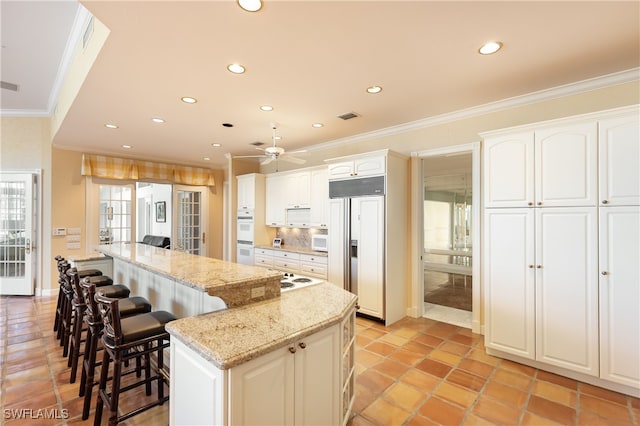 kitchen with light stone countertops, white cabinetry, a center island, paneled fridge, and crown molding