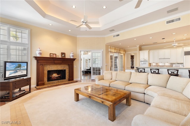 living room with a fireplace, light wood-type flooring, a tray ceiling, and ornamental molding