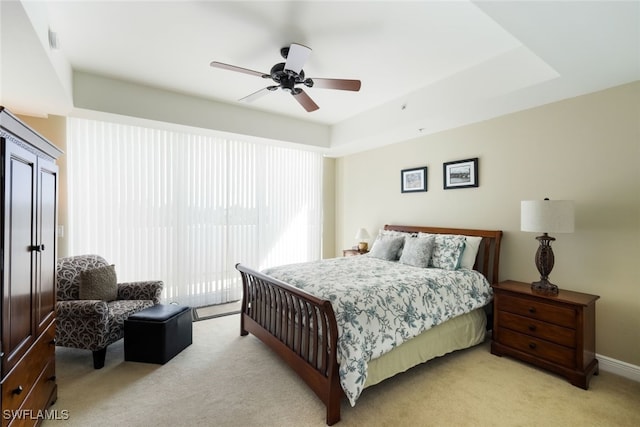 bedroom with a raised ceiling, ceiling fan, and light colored carpet