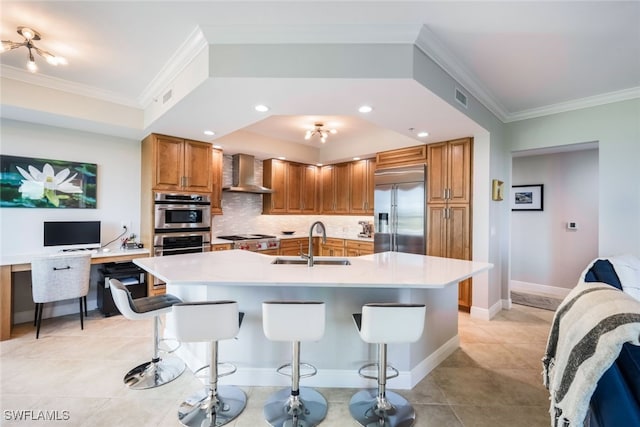 kitchen with sink, wall chimney exhaust hood, stainless steel appliances, a kitchen breakfast bar, and a kitchen island with sink