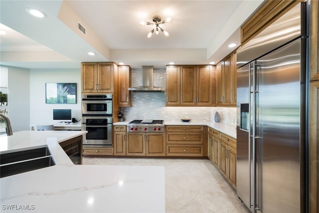 kitchen with decorative backsplash, light stone counters, stainless steel appliances, sink, and wall chimney range hood