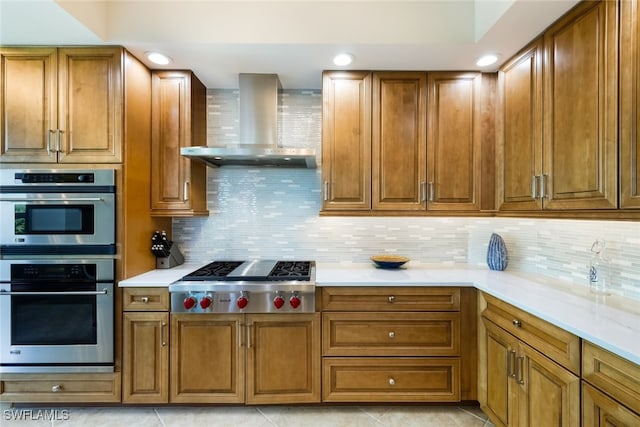 kitchen with light stone countertops, appliances with stainless steel finishes, backsplash, wall chimney range hood, and light tile patterned flooring