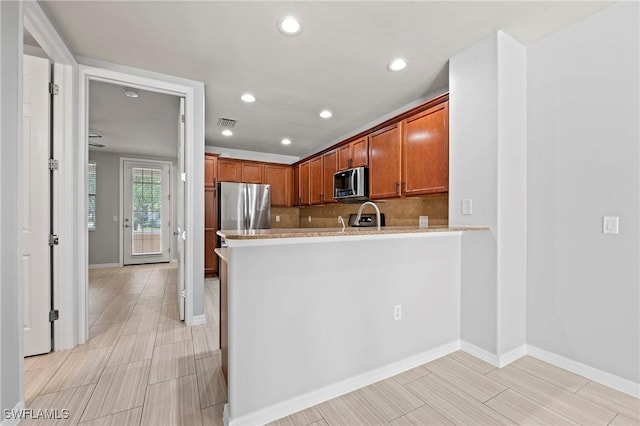 kitchen featuring light stone counters, appliances with stainless steel finishes, kitchen peninsula, and decorative backsplash