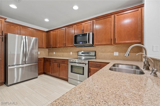 kitchen featuring light stone counters, appliances with stainless steel finishes, sink, and backsplash