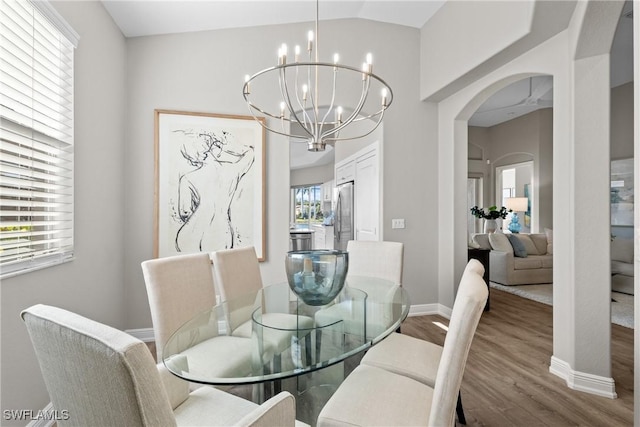 dining area with wood-type flooring, ceiling fan with notable chandelier, and lofted ceiling