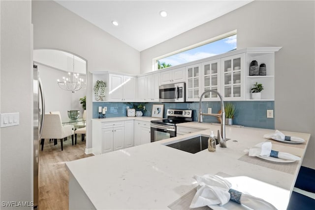 kitchen with pendant lighting, high vaulted ceiling, a notable chandelier, white cabinetry, and stainless steel appliances