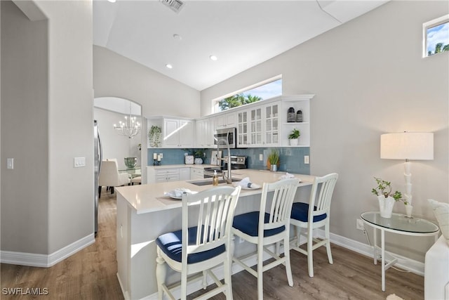 kitchen with kitchen peninsula, appliances with stainless steel finishes, sink, white cabinetry, and lofted ceiling