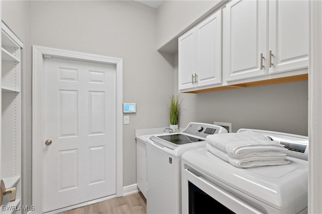 clothes washing area featuring washing machine and dryer, cabinets, and light wood-type flooring