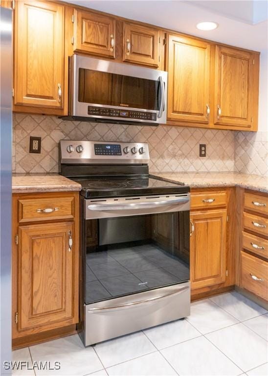 kitchen featuring backsplash, light stone countertops, light tile patterned floors, and stainless steel appliances