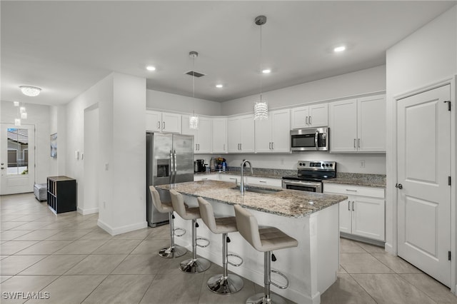 kitchen featuring stainless steel appliances, sink, a center island with sink, white cabinetry, and hanging light fixtures