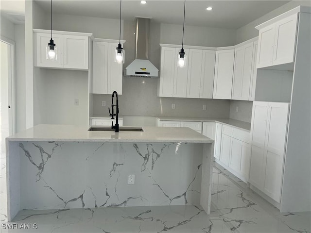 kitchen featuring white cabinets, wall chimney range hood, hanging light fixtures, and a kitchen island with sink