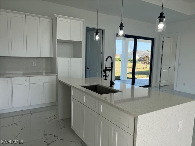 kitchen featuring a center island with sink, sink, light stone countertops, decorative light fixtures, and white cabinetry