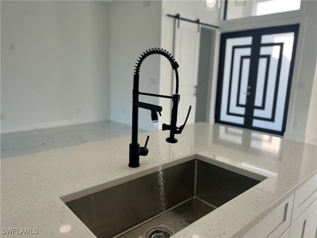 interior details featuring a barn door, a sink, white cabinets, and light stone countertops