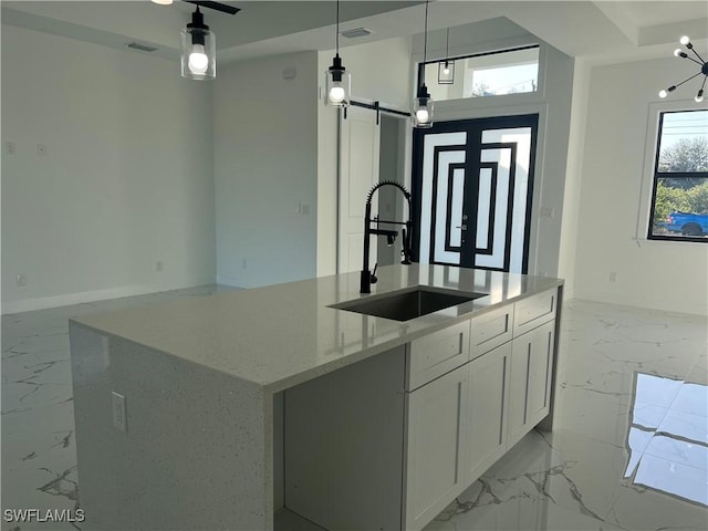 kitchen featuring pendant lighting, a center island with sink, a barn door, light stone countertops, and white cabinetry