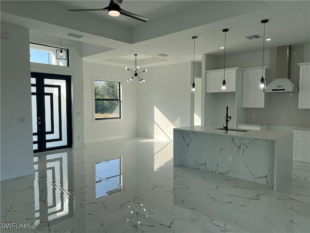 kitchen with white cabinets, a center island with sink, wall chimney range hood, and sink