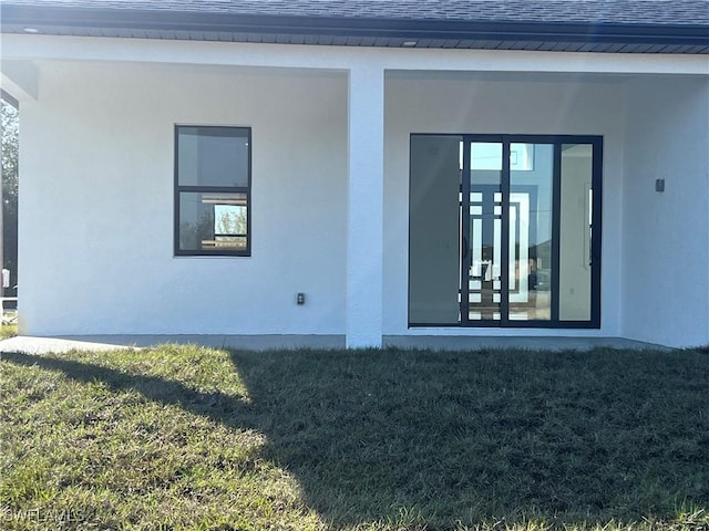 property entrance with roof with shingles, a yard, and stucco siding