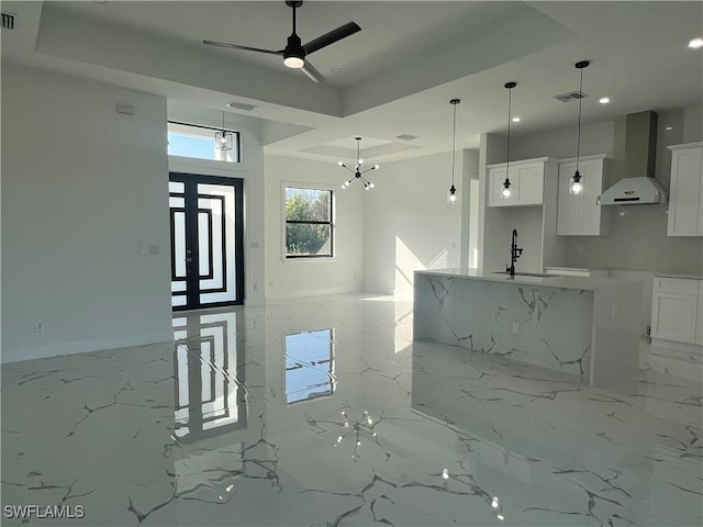 kitchen featuring decorative light fixtures, white cabinetry, wall chimney range hood, and sink