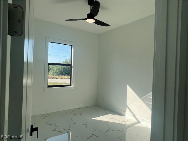 empty room featuring a ceiling fan, marble finish floor, and baseboards