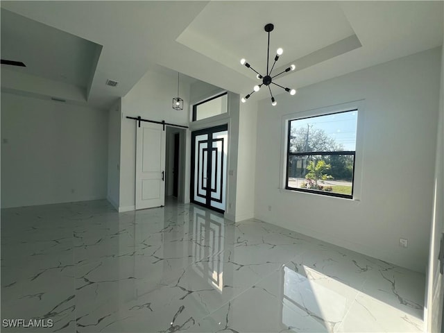 empty room featuring marble finish floor, a tray ceiling, a barn door, and visible vents